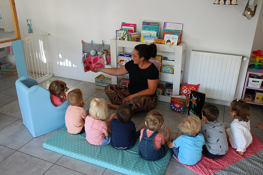 Assistant maternel, un métier fait pour vous ? À la Mam Au Bonheur des chouettes, Eugénie lit une histoire aux enfants assis devant elle.